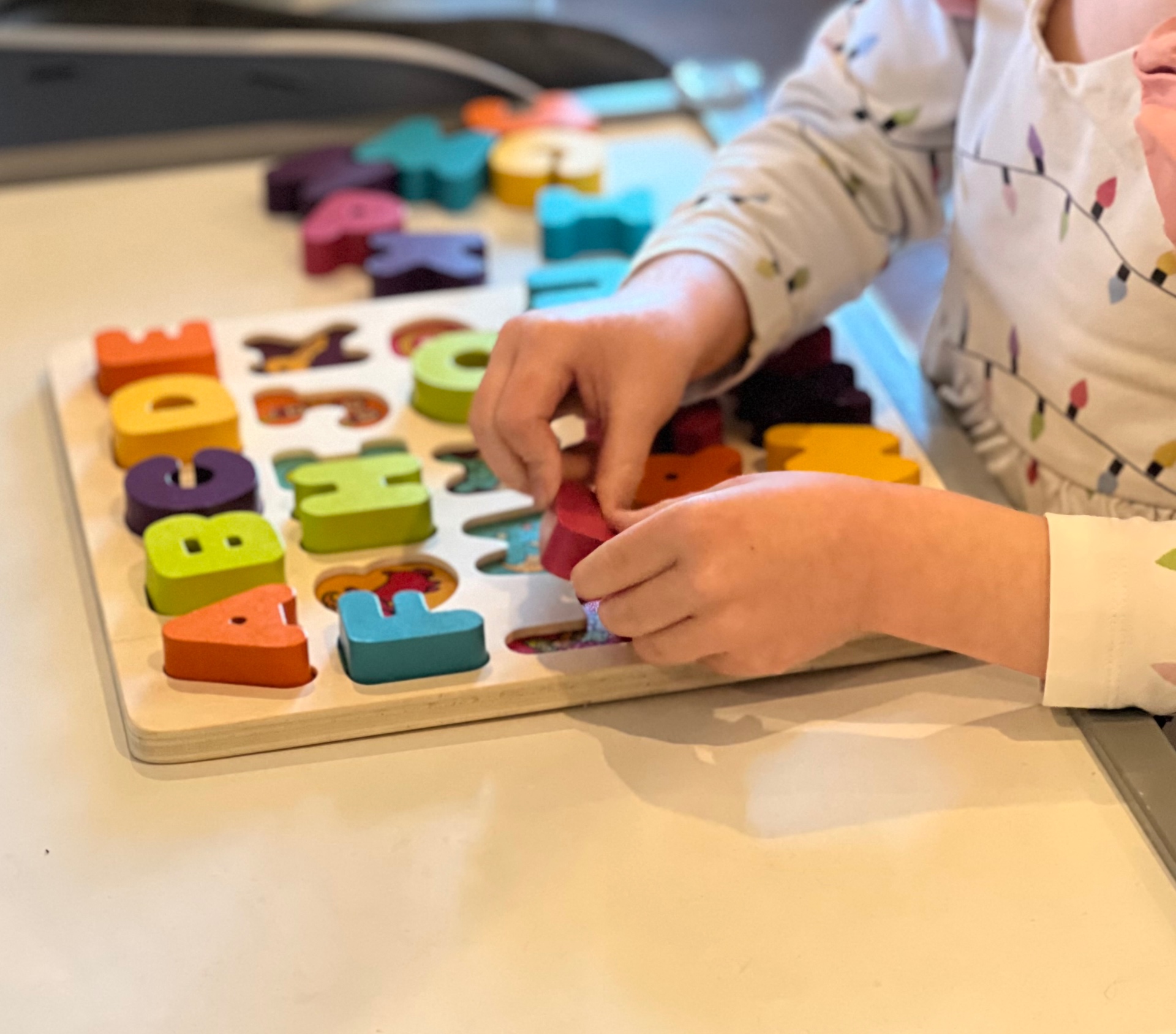 Small hands placing wooden letters into an alphabet board